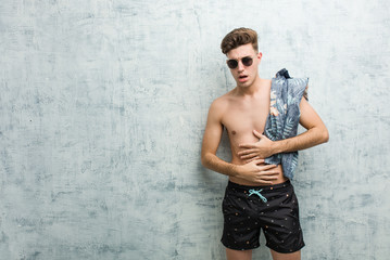 Young caucasian man wearing a swimsuit sick, suffering from stomachache, painful disease concept.