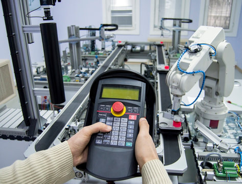 Man is pushing button on teach panel  to control a robotic arm which is integrated on smart factory production line. industry 4.0 automation line which is equipped with sensors and robotic arm.