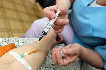 The nurse enters a medical syringe into the system of tubes in the hand of a woman who is lying. The concept of medical procedure.
