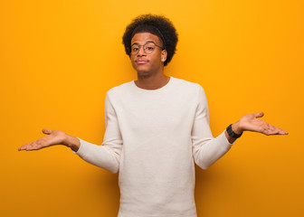 Young african american man over an orange wall doubting and shrugging shoulders