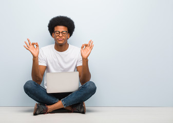 Young black man sitting on the floor with a laptop performing yoga