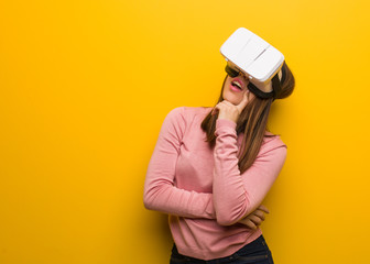 Young cute woman wearing a virtual reality googles relaxed thinking about something looking at a...