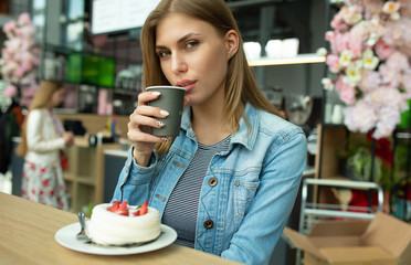 Gorgeous smiling young woman eating cake and drinking coffee at a cafeteria 