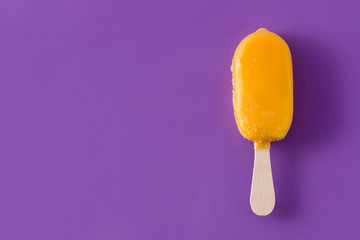 Orange popsicle on violet background. Top view. Copyspace