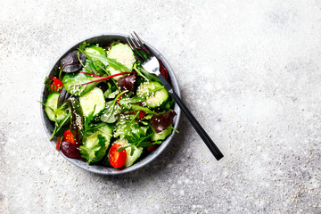 Vegetable salad in a glass bowl with greens, olive oil and sesame  on a gray background.Vegetarian. Concept for a tasty and healthy meal. Copy space for Text.Top view.