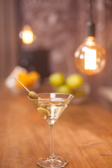 A glass of martini on a bar counter with fruits blured in the background