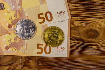 Fifty euro banknotes and bitcoins on wooden background. Top view