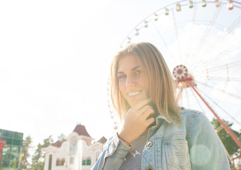 Close up of a smiling relaxed young blond looking away at the park Ferris wheel on background. Happy woman in sunlight