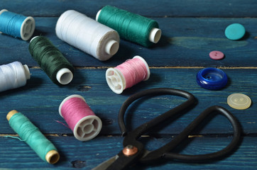 Colorful bobbins of thread on a blue wooden background. Black old scissors