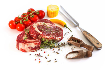 set for cooking a festive dinner for two. two raw marbled beef steaks, spices, vegetables and a grill pan with a meat fork. all on a white background