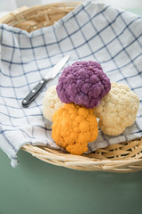 Bunter Blumenkohl in Lila, Orange und Weiß auf Geschirrtuch mit Messer in Korb auf Pastell Mint...