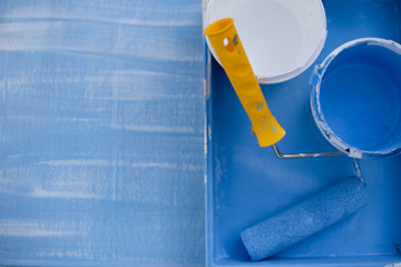blue and white paint in cans top view. roller with a yellow handle for painting walls