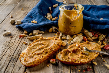 Little peanut butter jar with crunchy peanut butter sandwiches on rustic wooden table