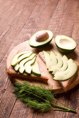 Beautifully plated avocado toast with delicious-looking toppings on wooden brouw background. Making sandwiches with avocado healthy organic food top view.On A Wooden Cutting Board Sliced avocado.