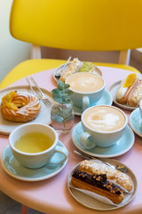 Cafe table with cups of coffee, eclairs and cake