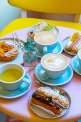 Cafe table with cups of coffee, eclairs and cake