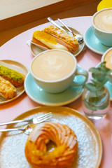 Cafe table with cups of coffee, eclairs and cake