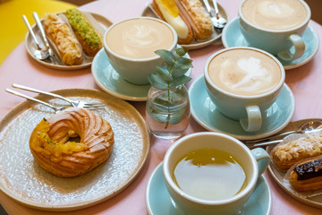 Cafe table with cups of coffee, eclairs and cake