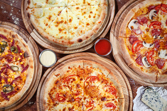 Top view on different fresh italian pizzas on wooden background with copy space for logo or design. View from above on table with many pizza with decoration. Flat lay