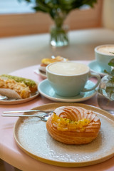 Cafe table with cups of coffee, eclairs and cake