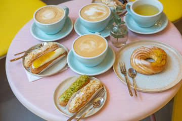 Cafe table with cups of coffee, eclairs and cake