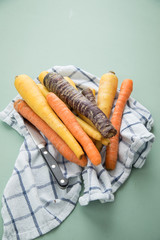 Bunte Urkarotte und Möhren in Lila, Orange und Gelb auf Geschirrtuch mit Messer auf Pastell Mint Grün Hintergrund