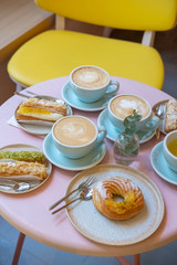 Cafe table with cups of coffee, eclairs and cake