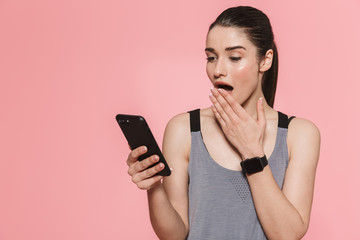 Amazing beautiful young pretty fitness woman using mobile phone isolated over pink wall background.