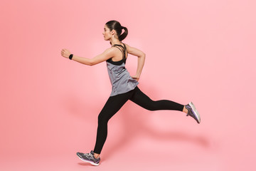 Beautiful young pretty fitness woman running make sport exercises isolated over pink wall...