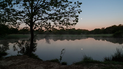 Full moon at daybreak, still waters with reflections
