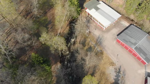 Drone footage flying high above a fast flowing stream of white foamed water with trees and a building in sight. Filmed in realtime at 4K.