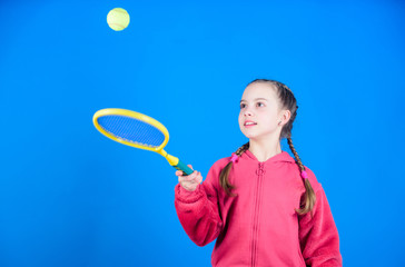 Girl adorable child play tennis. Practicing tennis skills and having fun. Athlete kid tennis racket on blue background. Active leisure and hobby. Tennis sport and entertainment. Focused on ball