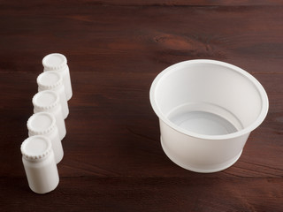 Five small plastic white banks with lids and one large bank on a brown wooden background