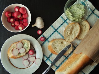 Fresh white baguette and a glass bowl with green butter made of butter, dill, garlic and salt and white bowl with organic radish, slice of baguette with green butter and sliced radish. Healthy food.