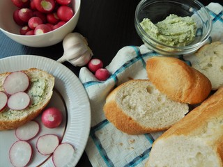 Fresh white baguette and a glass bowl with green butter made of butter, dill, garlic and salt and white bowl with organic radish, slice of baguette with green butter and sliced radish. Healthy food.