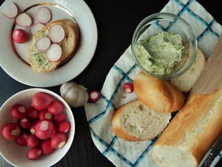 Fresh white baguette and a glass bowl with green butter made of butter, dill, garlic and salt and white bowl with organic radish, slice of baguette with green butter and sliced radish. Healthy food.