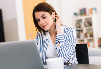 Businesswoman with headphones using laptop and listening music at home