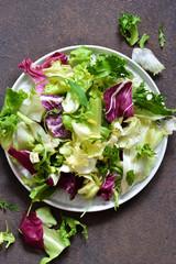 Fresh mix of salads: lettuce, arugula, spinach, mesclun, mache on a dark background. Top view.