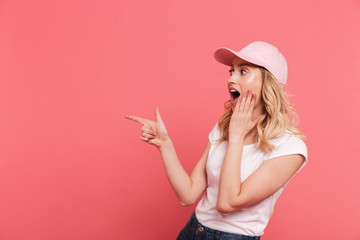 Portrait of trendy blond woman 20s wearing casual t-shirt and cap pointing fingers aside at copyspace