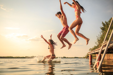 A group of young people joyfully leap into the refreshing lake waters on a sunny summer day,...