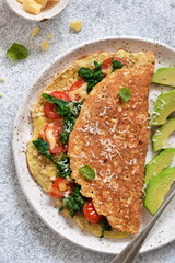 Omelet with tomatoes, cheese and basil in a plate on the kitchen table. View from above.