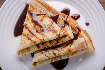 Flat lay French crepes with chocolate sauce in ceramic dish on wooden kitchen table