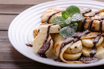French crepes with chocolate sauce and banana in ceramic dish on wooden kitchen table