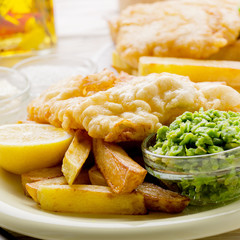Traditional British street food fish and chips with tartar sauce and mushy peas on paper plate