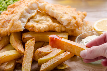 Traditional British street food fish and chips with ketchup sauce and lemon on bakery paper
