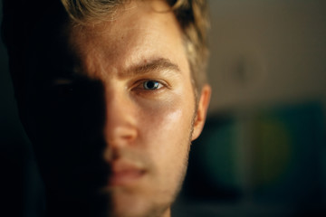 Serious man portrait in light on dark background. Closeup of man face with blue eyes and blonde hair in softlight. Selective focus. Creative image - Powered by Adobe