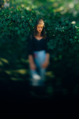 Obraz na płótnie Canvas Stylish hipster girl posing at green leaves bush, atmospheric moment. Fashionable woman in denim jeans and black shirt relaxing in park. Selective focus, creative image. Space for text