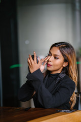 Portrait of an attractive, sophisticated, professional Southeast Asian woman, manager or an entrepreneur in a business suit putting on her foundation, mascara and blusher before her business meeting.