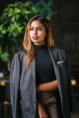 Fototapeta premium Mid shot Portrait of a tanned,professional young Southeast Asian business woman in a dark turtle neck blouse with blazer and slacks standing in the city restaurant and is looking away from the viewer.