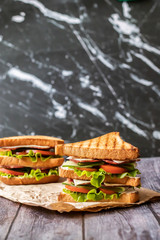 Sandwich with cheese, tomato, cucumber, sausage and lettuce on a wooden background. Vertical orientation